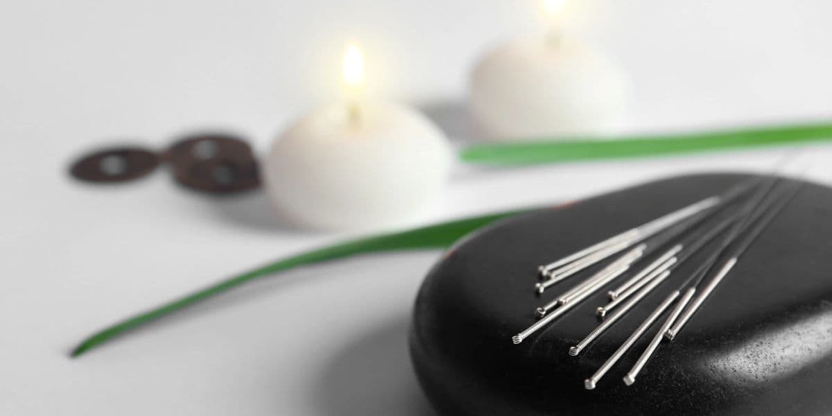 Acupuncture needles beside stones and a lit candle for fertility treatment